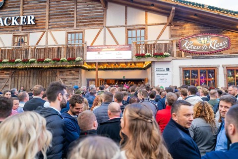 A large crowd waits outside in front of a festively decorated wooden house, Cannstatter Wasen fair,