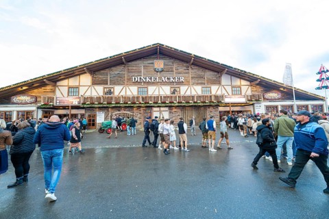 Visitors move in front of a large wooden building, lively atmosphere, Cannstatter Wasen folk