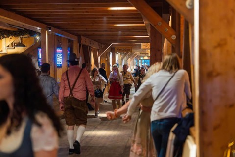 People in traditional dress walk through a corridor in a venue, Cannstatter Wasen folk festival,