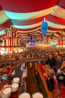 People celebrating at a long table in a colourful striped marquee, Cannstatter Wasen folk festival,