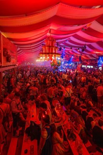 Lively celebration with intense red lighting in a marquee, Cannstatter Wasen folk festival,