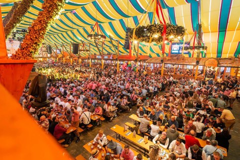 Large crowd celebrating in a colourfully decorated marquee, Cannstatter Wasen folk festival,