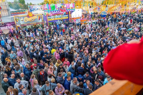 Dense crowd on a busy fairground with colourful attractions all around, Cannstatter Wasen funfair,