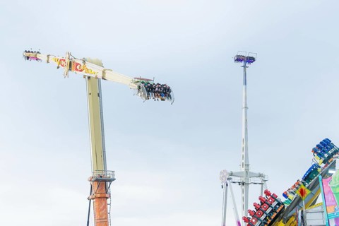 View of thrill rides with people high above and other attractions in the background, Cannstatter