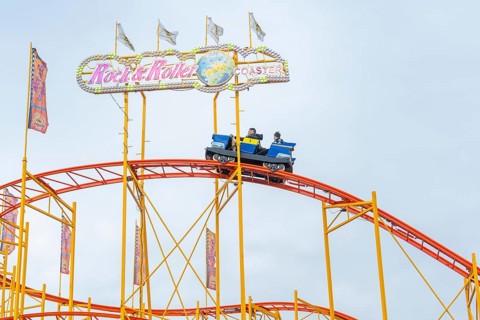 Colourful roller coaster with brave passengers on the rails in the amusement park, Cannstatter
