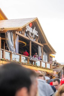 People standing on a balcony of a Bavarian wooden building with a glass front, Cannstatter Wasen