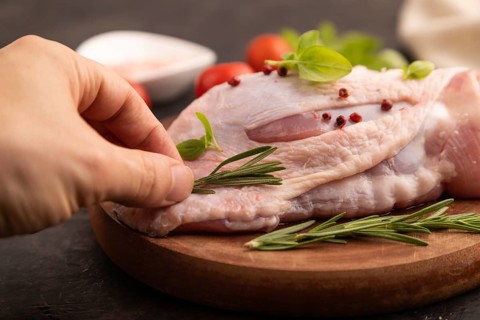 Raw Turkey Thigh with spices and rosemary on cutting board on black concrete background with hand