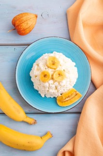 White ?ottage cheese, Curd, with Banana on blue wooden background and orange textile, top view,