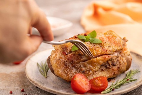 Fried Turkey Thigh with spices and rosemary on plate with hand on brown concrete background and