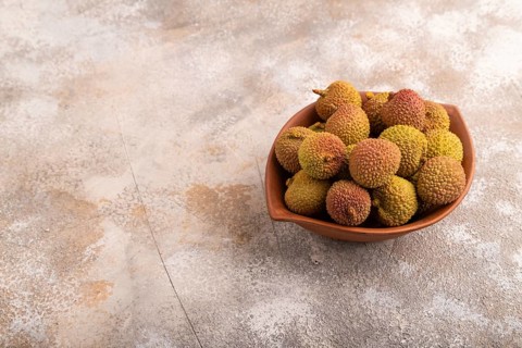 Ripe Lychee on clay bowl on brown concrete background, side view, copy space, minimalism