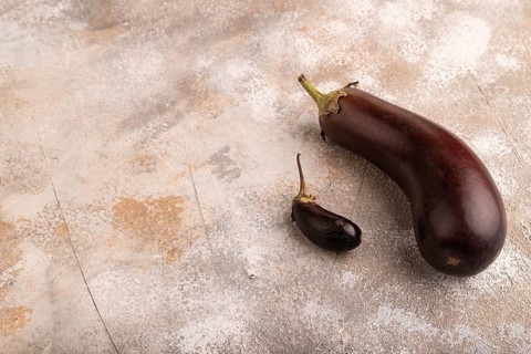 Two Eggplants big and small on brown concrete background, side view, copy space, minimalism