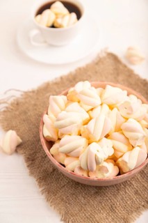 Orange and pink marshmallow in ceramic bowl on white wooden background, side view, close up,