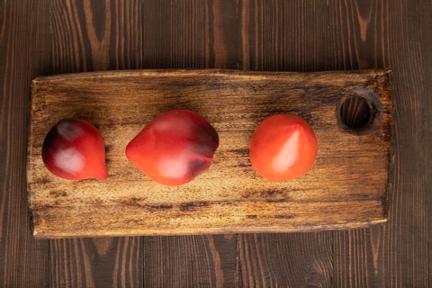 Red Heart shape tomatoes on cutting board on brown wooden background. Top view, copy space, flat