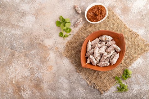 Small smoked Chicken sausages in clay bowl on brown concrete background and linen textile. top