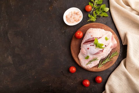 Raw Turkey Thigh with spices and rosemary on cutting board on black concrete background and linen