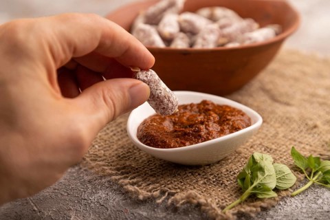 Small smoked Chicken sausages in clay bowl with hand on brown concrete background and linen textile