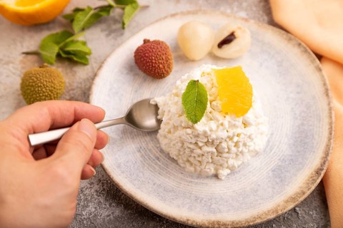 White ?ottage cheese, Curd, with orange and lychee with hand on brown concrete background and