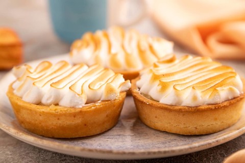 French lemon tart with meringue on brown concrete background, cup of coffee, orange linen textile,