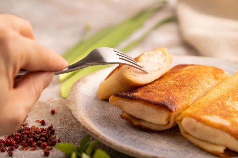 Fried crispy pancakes with meat and cheese with hand on brown concrete background and linen textile