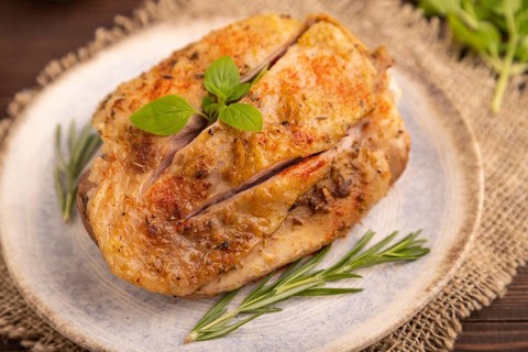 Fried Turkey Thigh with spices and rosemary on plate on brown wooden background and linen textile.