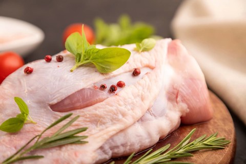 Raw Turkey Thigh with spices and rosemary on cutting board on black concrete background and linen