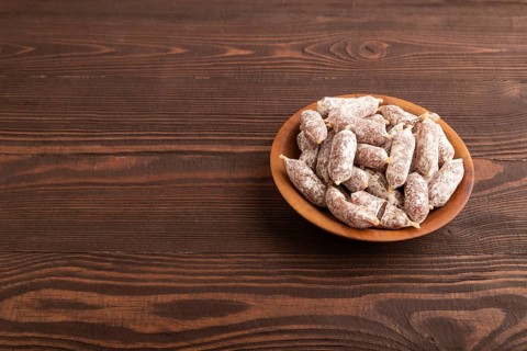 Small smoked Chicken sausages in wooden bowl on brown wooden background. side view, copy space