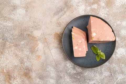 Mortadella sausage on plate with pepper and herbs on brown concrete background. Top view, flat lay,