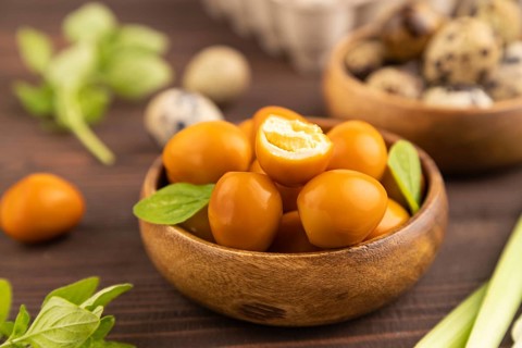 Pile of Smoked Quail eggs in bowl on a brown wooden background. side view, close up, selective