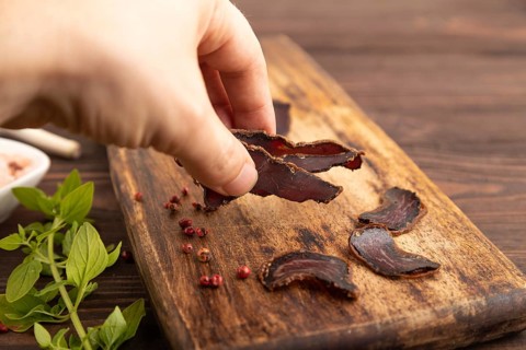 Armenian Basturma dried meat with hand on wooden cutting board with pepper and herbs on brown