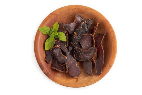 Armenian Basturma dried meat on wooden bowl isolated on white background. Top view, flat lay