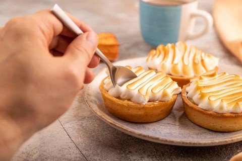 French lemon tart with meringue with hand on brown concrete background, cup of coffee, orange linen