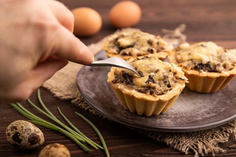 Tartlets with meat and cheese with hand on brown wooden background and linen textile. side view,