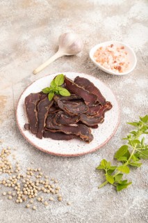Armenian Basturma dried meat on plate with pepper and herbs on brown concrete background. Side
