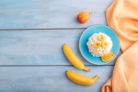 White ?ottage cheese, Curd, with Banana on blue wooden background and orange textile, top view,