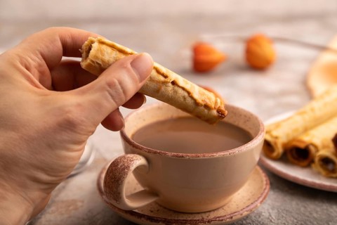 Waffles with caramel with hand on brown concrete background and orange linen textile, side view,