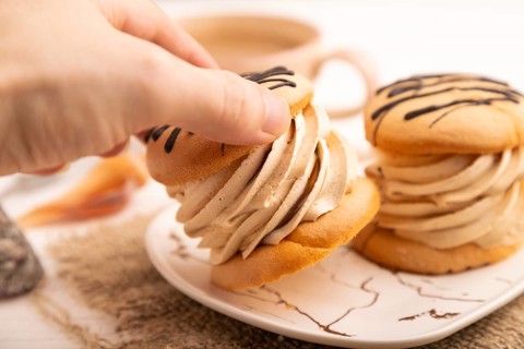 Caramel Cream Cakes with hand on white wooden background and linen textile, cup of coffee, side