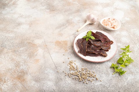 Armenian Basturma dried meat on plate with pepper and herbs on brown concrete background. Side