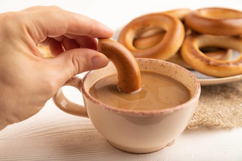 Homemade Ring Bagel with hand with cup of coffee on white wooden background and linen textile. side