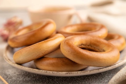 Homemade Ring Bagel with cup of coffee on brown concrete background and linen textile. side view,