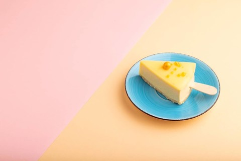 Yellow Cake pop with sprinkles on blue ceramic plate on pink and orange pastel paper background,