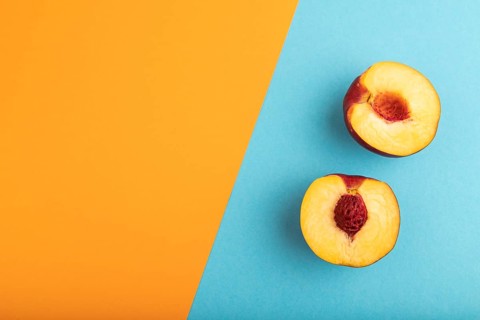 Peach Cut in half on orange and blue paper pastel background. Top view, flat lay, copy space.