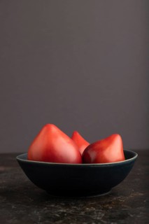 Red Heart shape tomatoes in blue bowl on black concrete background. Side view, copy space. healthy
