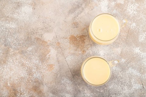Organic non dairy banana and soy milk in glass on brown concrete background. Vegan healthy food