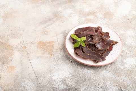 Armenian Basturma dried meat on plate with pepper and herbs on brown concrete background. Side