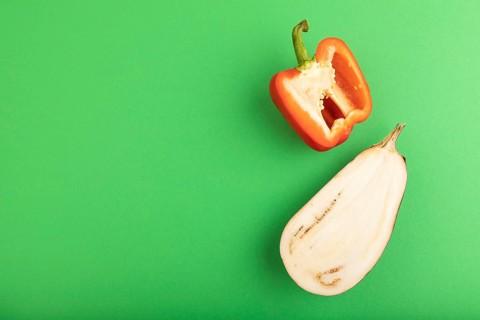 Red Cutted pepper and Purple Cutted eggplant on green pastel background. Top view, flat lay, copy