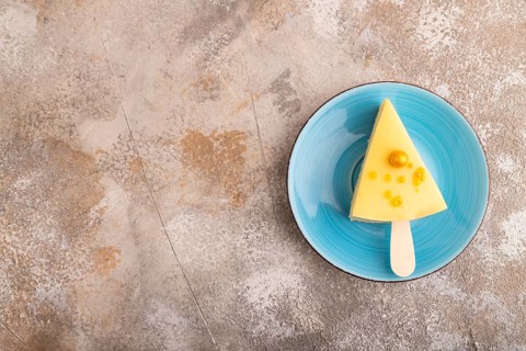 Yellow Cake pop with sprinkles on blue ceramic plate on brown concrete background, top view, flat