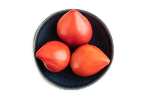 Red Heart shape tomatoes in blue bowl isolated on white background. Top view, copy space, flat lay.