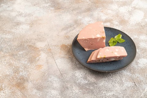 Mortadella sausage on wooden cutting board with pepper and herbs on brown concrete background. Side