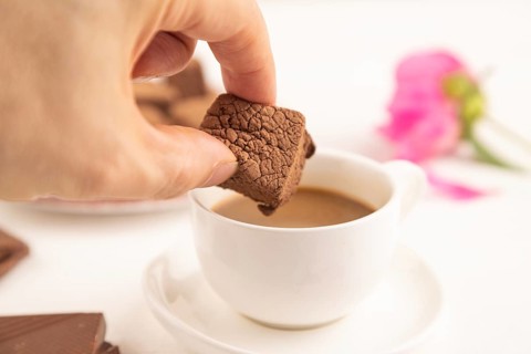 Chocolate marshmallow with cup of coffee with hand on white wooden background. side view, close up,