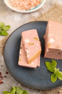 Mortadella sausage on plate with pepper and herbs on brown concrete background and linen textile.